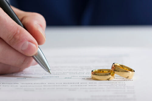 A person signing a divorce settlement with two wedding bands