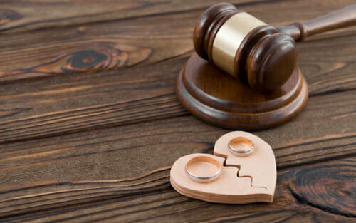 A gavel and two wedding rings on a broken, wooden heart to dignify divorce in Maryland. 