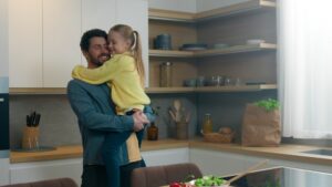 Adult father man dad holding little lovely cute daughter at kitchen happy family hugging. Child kid girl and daddy hug tender enjoy moment bonding good relationship together at home cooking custody